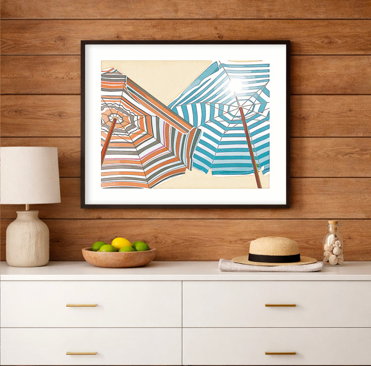 Colorful beach umbrellas viewed from below against a bright blue sky, coastal art print displayed in a light beach house interior