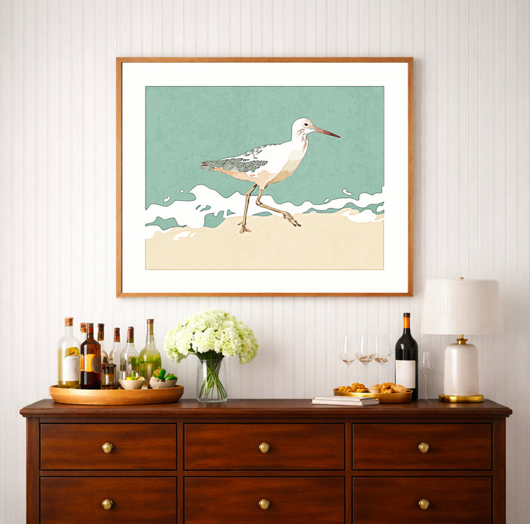 Sandpiper walking along the shoreline at low tide, coastal bird art print displayed in a neutral beach-style interior