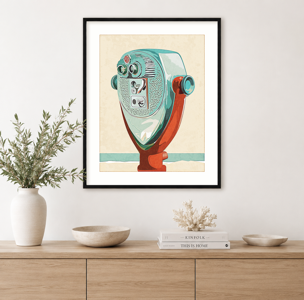 Framed vintage-inspired coin-operated beach binocular viewer wall art print displayed above a modern light oak console in a bright coastal interior.